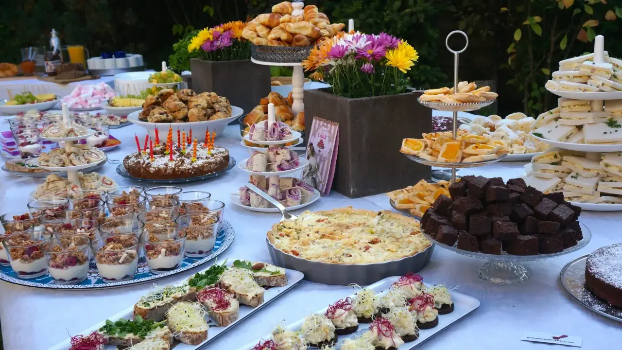 Ein üppiges Brunch Buffet im Freien mit Croissants, Quiche, Brownies, Sandwiches und süßen Leckereien.