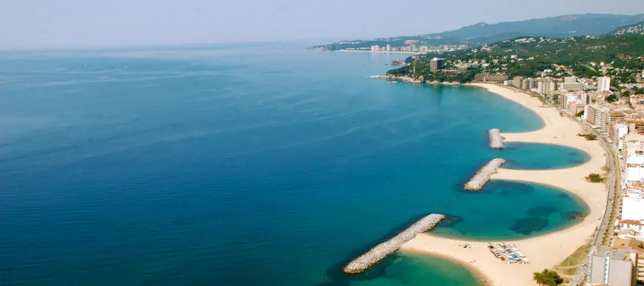 Bucht mit Wellenbrechern und Sandstränden in Calonge, Spanien. Die Küstenstadt erstreckt sich entlang des blauen Meeres.
