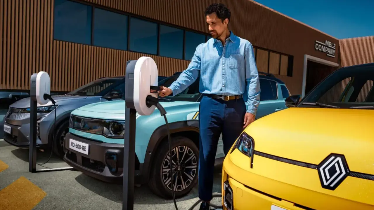 Un homme charge une automobile hybride électrique turquoise. Une voiture jaune est garée à côté.
