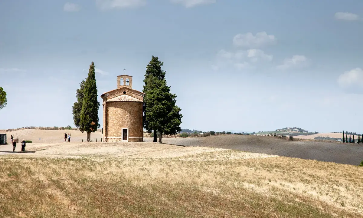Cappella della Madonna di Vitaleta, icona della Val d'Orcia, circondata da cipressi e dolci colline toscane sotto un cielo azzurro.
