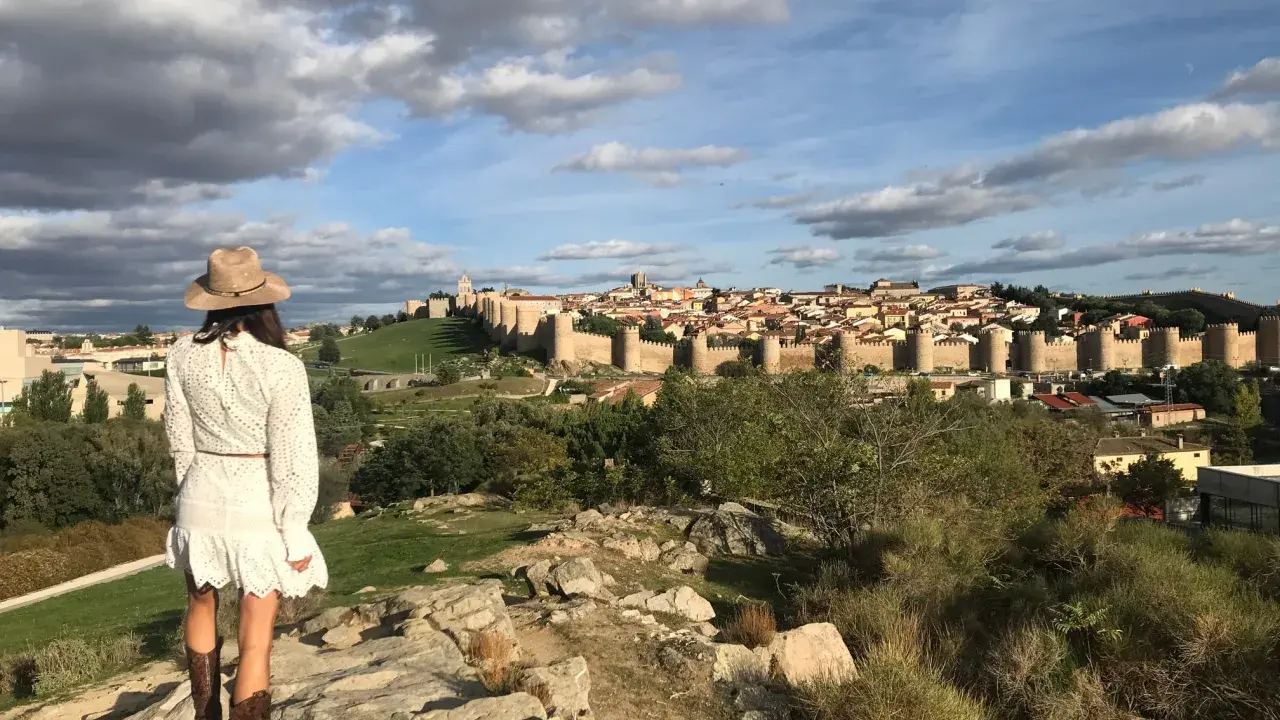 Mujer con sombrero y botas de cowboy admira las murallas de Ávila, un lugar perfecto para visitar con niños.