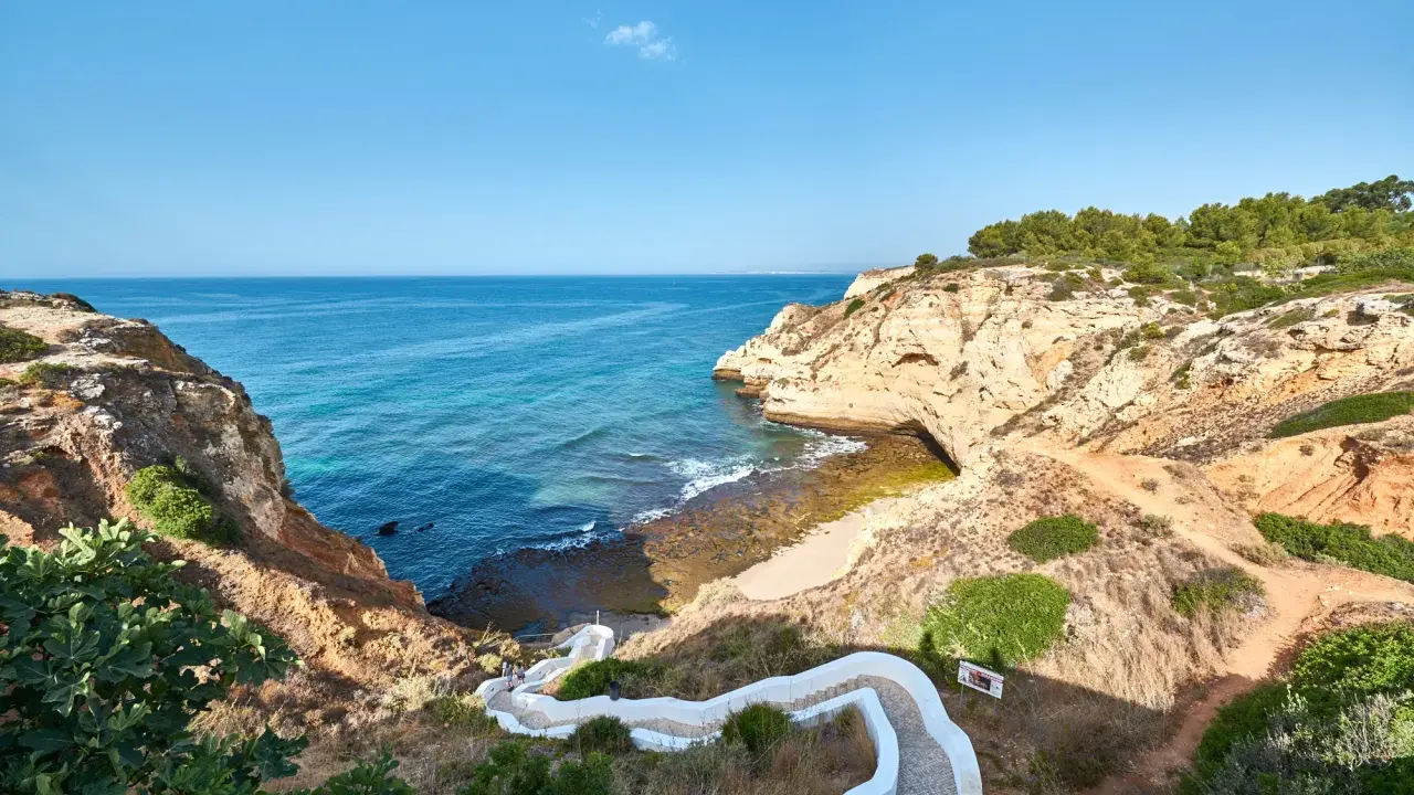 Treppe führt zum malerischen Algarve Meer. Felsformationen und türkisfarbenes Wasser.
