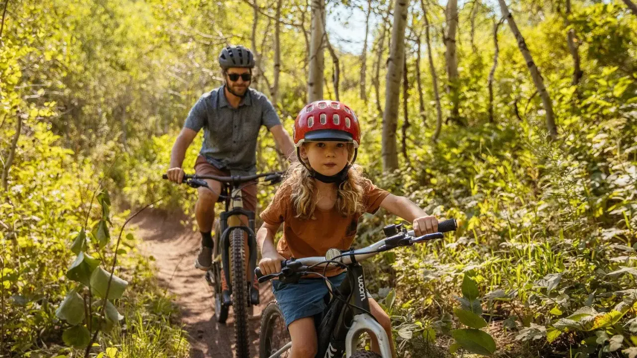 En flicka och en man cyklar på en stig i en lummig skog. Solen lyser genom träden och skapar ett vackert ljusspel.