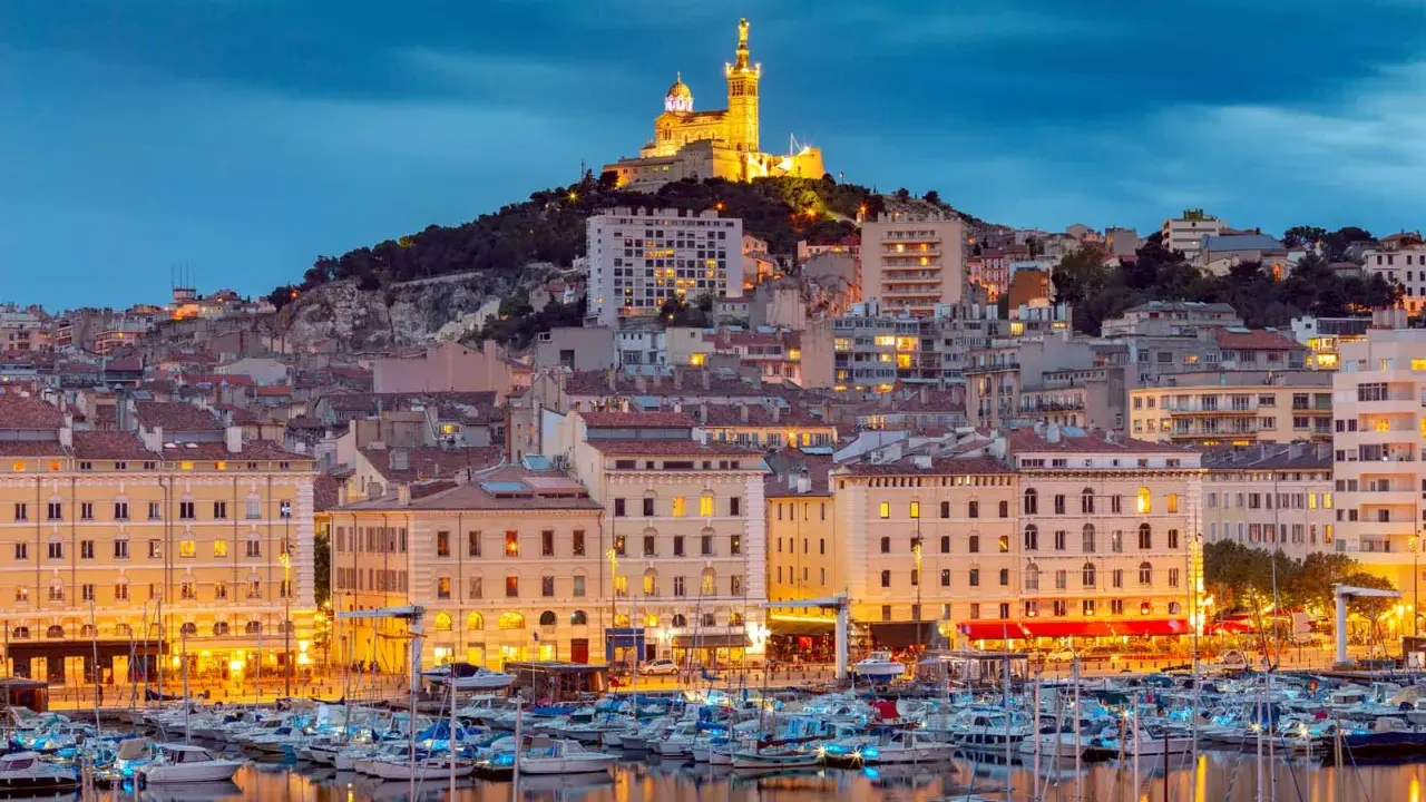Il porto di Marsiglia MSC, con le luci della città e la basilica di Notre-Dame de la Garde in cima alla collina, crea uno scenario suggestivo al crepuscolo.