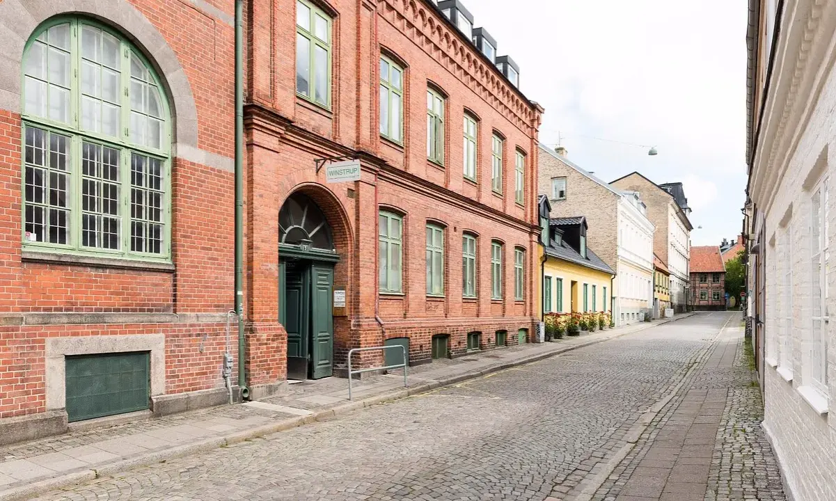 Gammalt tegelhus med gröna fönster och dörrar, en del av ett charmigt vandrarhem i Skåne. Gatsten leder längs en lugn gata.