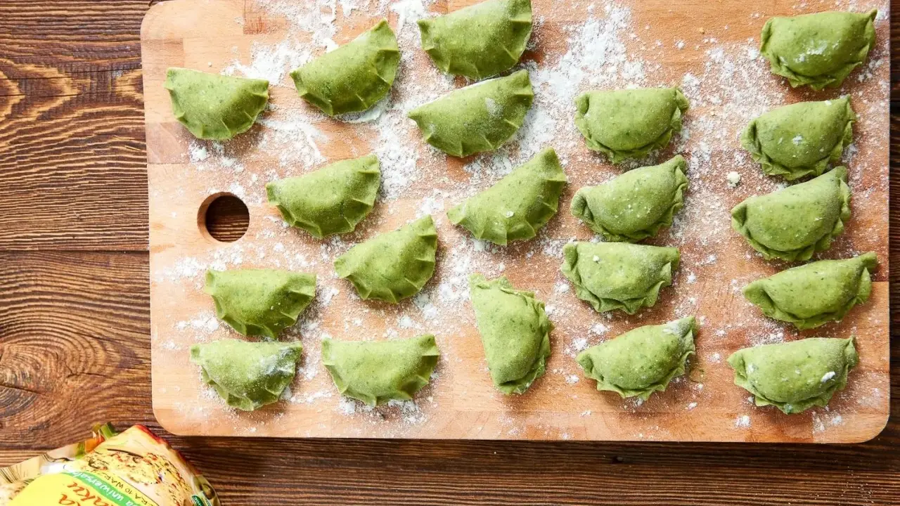 Zielone pierogi ze szpinakiem ułożone na desce, posypane mąką. Czekają na gotowanie.