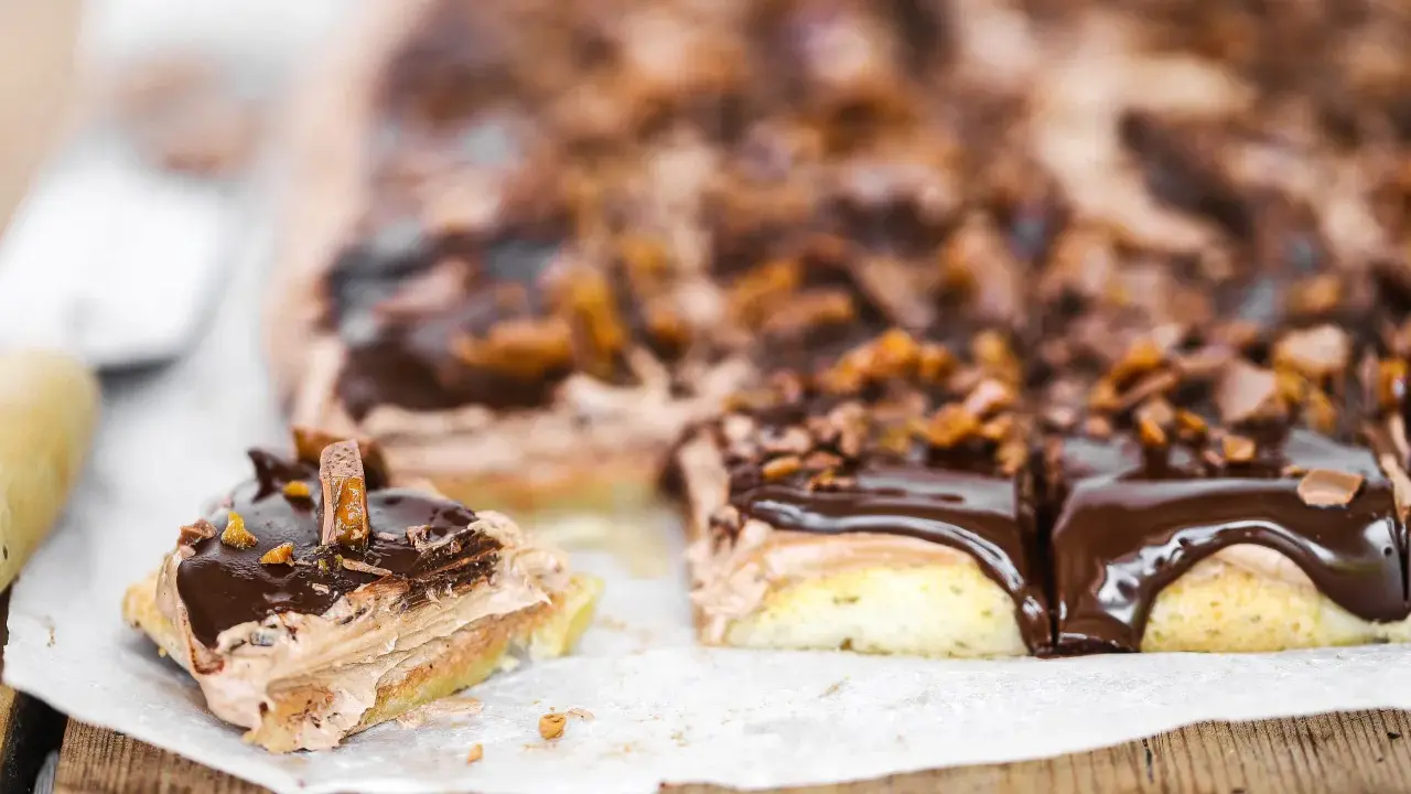 En chokladkaka i långpanna med fluffig chokladkräm och glansig chokladglasyr, toppad med krossad choklad och bitar av godis.