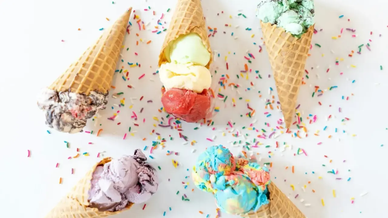 Cinco conos de helado de chuche de colores vibrantes, esparcidos con confeti sobre fondo blanco.