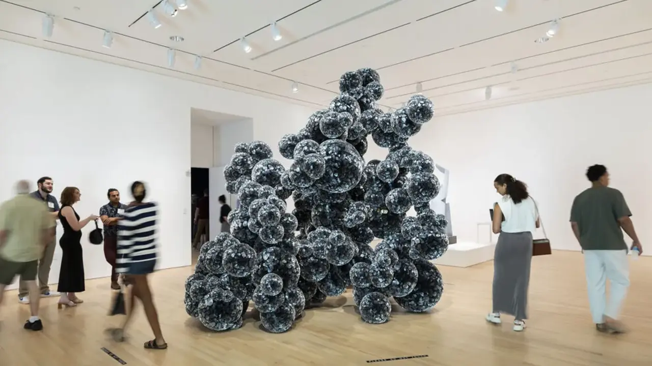 Visitors admire a large, dark, spherical sculpture in a bright gallery space, typical of Indianapolis Museum of Art photos.