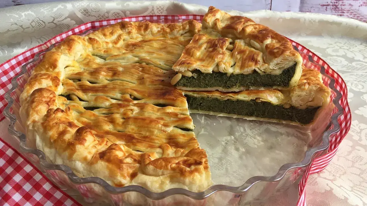 Torta salata ricotta e spinaci dorata e invitante, con una fetta tagliata che mostra il ripieno verde e cremoso.