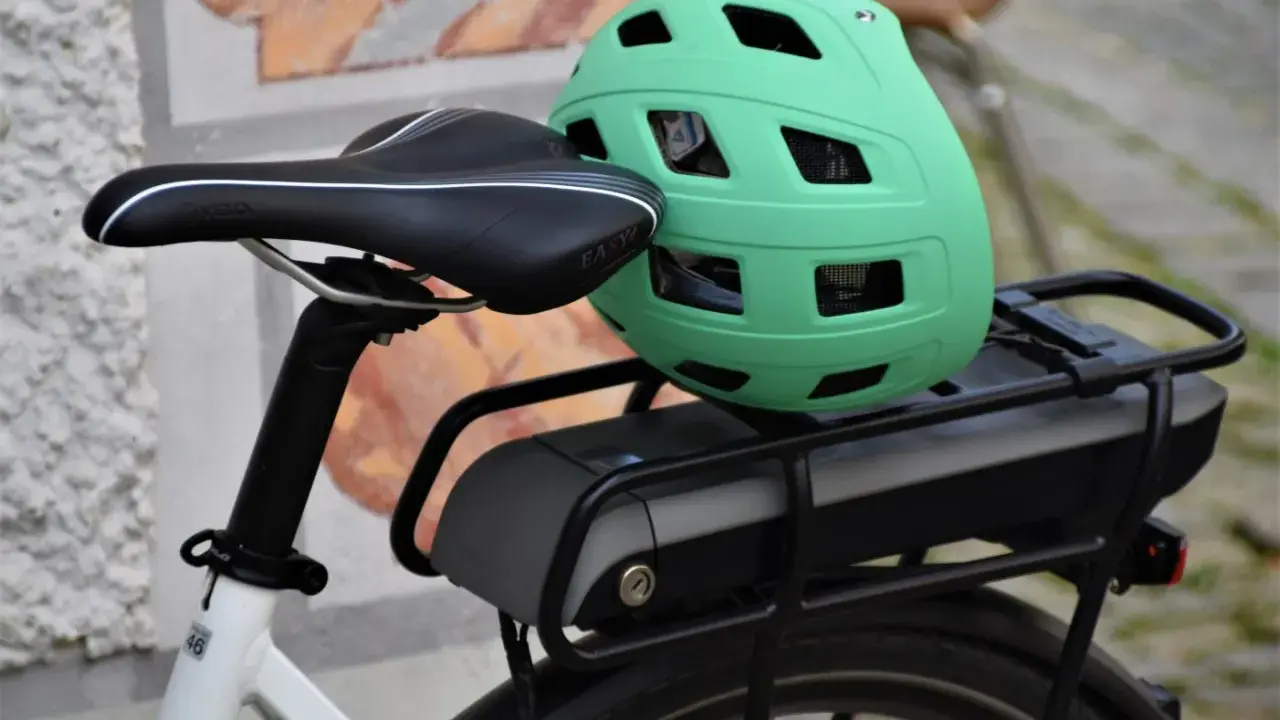 Zielony kask na bagażniku roweru elektrycznego, obok siodełka. Baterie do rowerów elektrycznych są gotowe do długiej podróży.