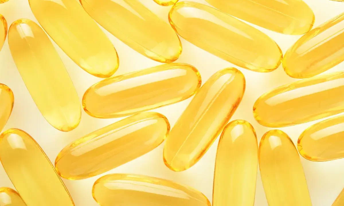 Żółte kapsułki omega 3 ułożone na jasnym tle. Kiedy brać omega 3? Najlepiej po posiłku, by zwiększyć wchłanianie.