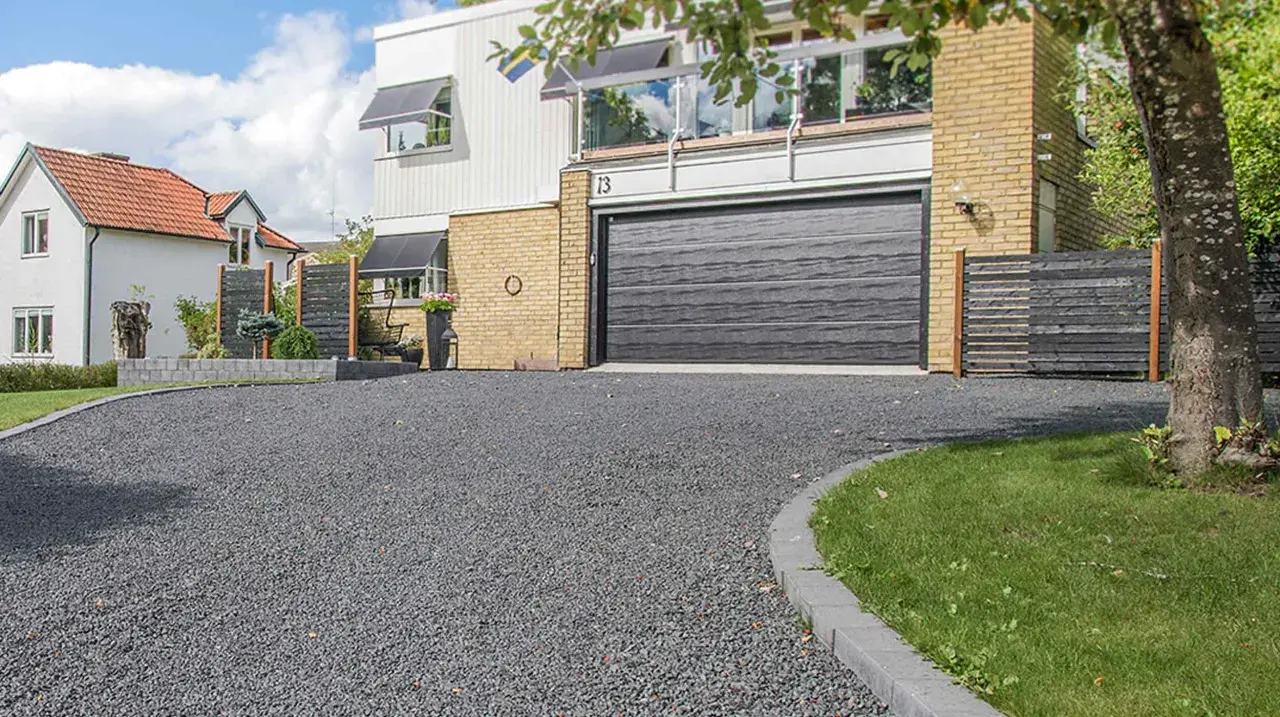 En vacker grusgång leder fram till ett modernt hus med garage. Gruset ger en stilren och praktisk yta.