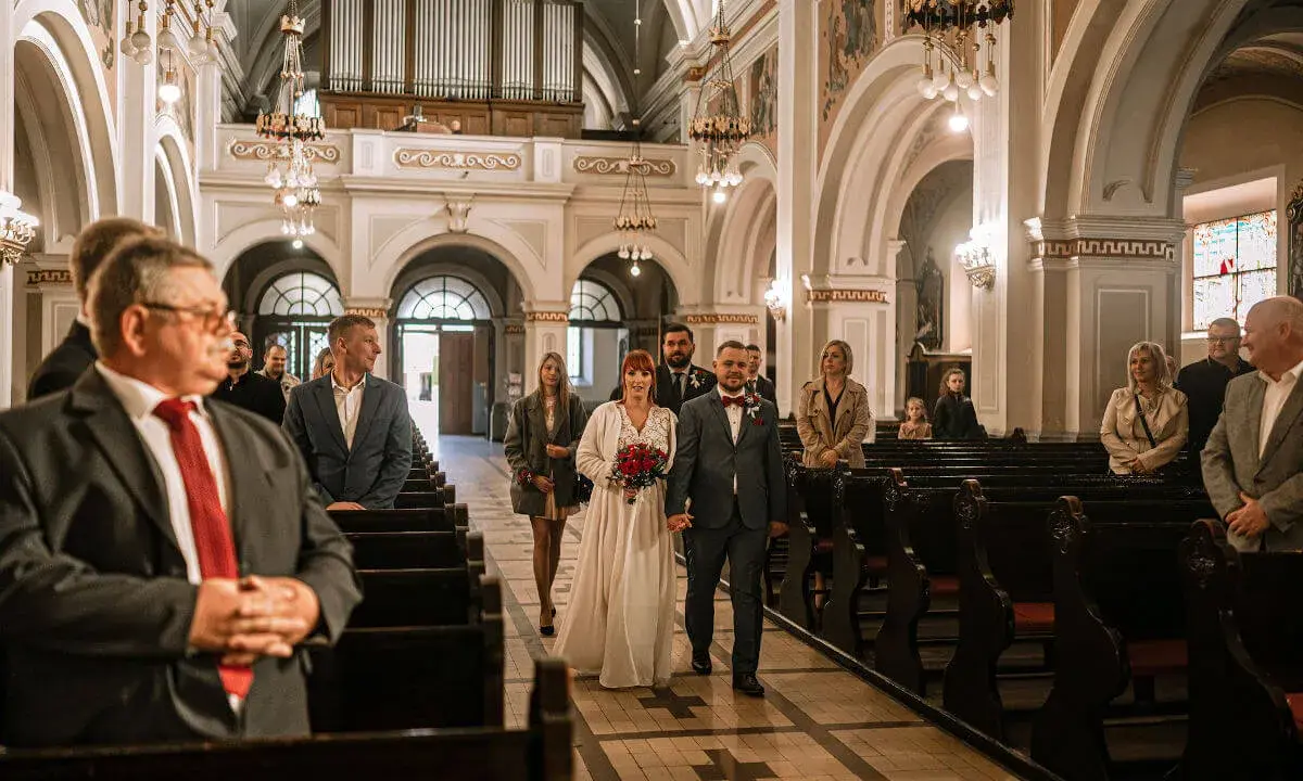 Para młoda idzie do ołtarza przy akompaniamencie piosenki na wejście. W kościele zgromadzeni goście.