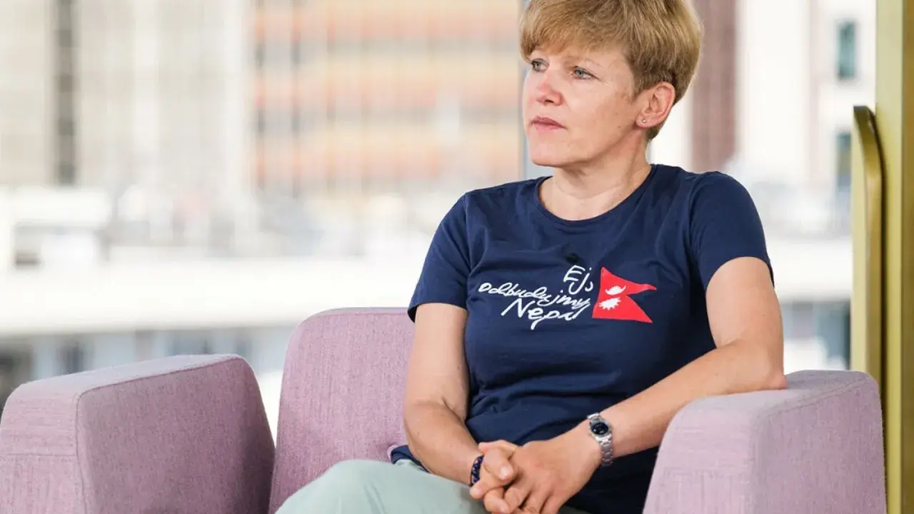 Monika Witkowska w granatowej koszulce z napisem "Odbudujmy Nepal" siedzi w różowym fotelu, patrząc w bok.