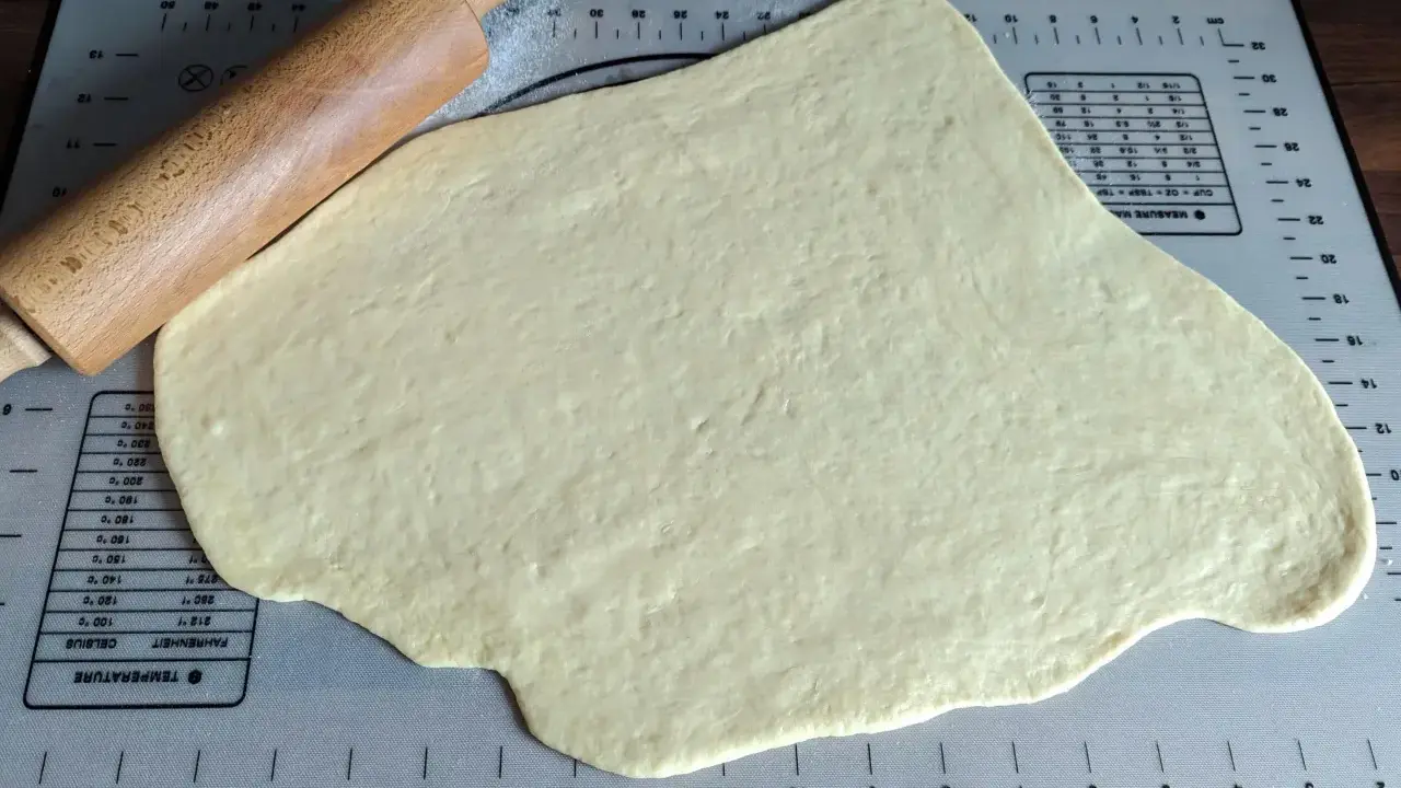 Pâte à beignet légère et croustillante étalée sur un tapis de pâtisserie avec un rouleau à pâtisserie en bois.