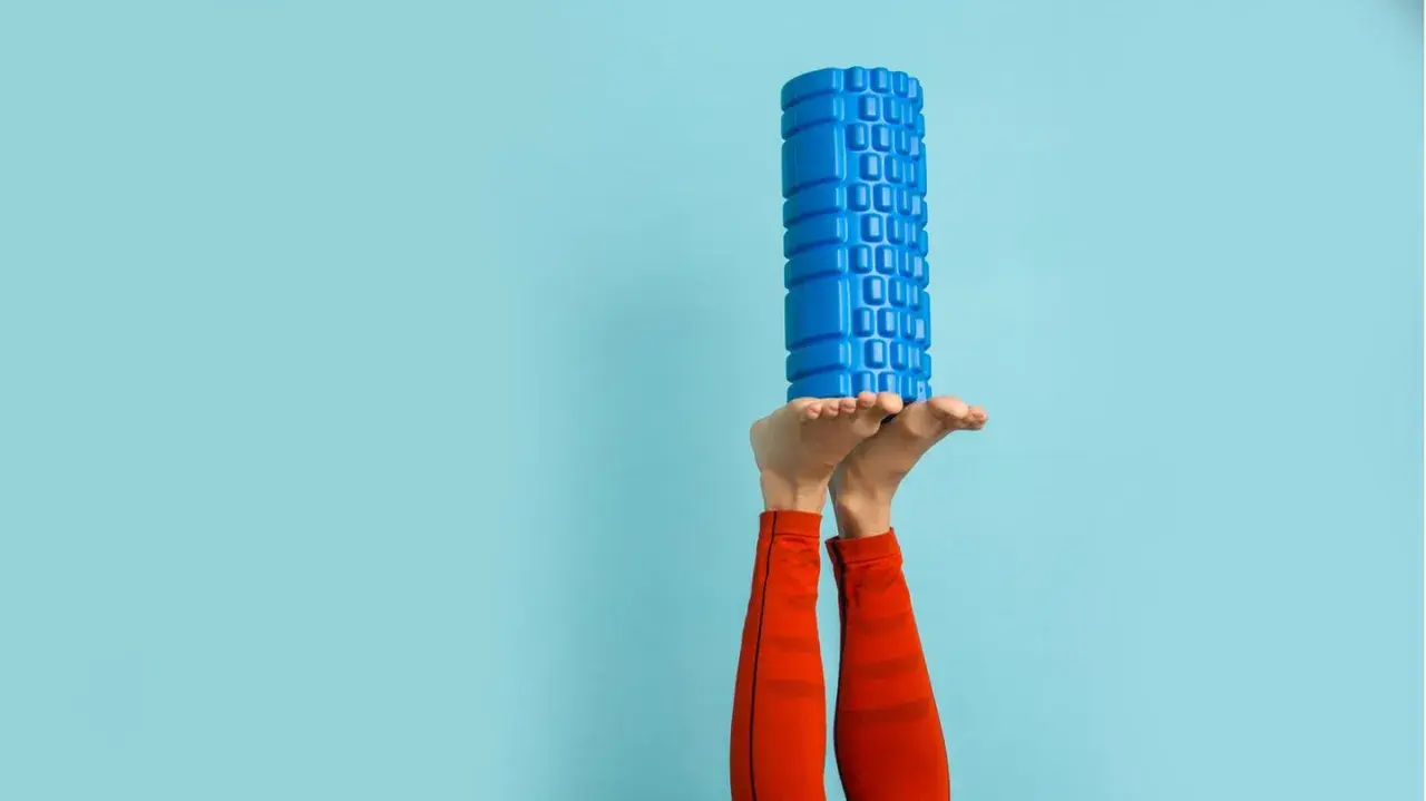 Beine in der Luft, ein blauer Faszienroller balanciert auf den Füßen. Ein Zeichen für das effektive Faszien entgiften und Regeneration.