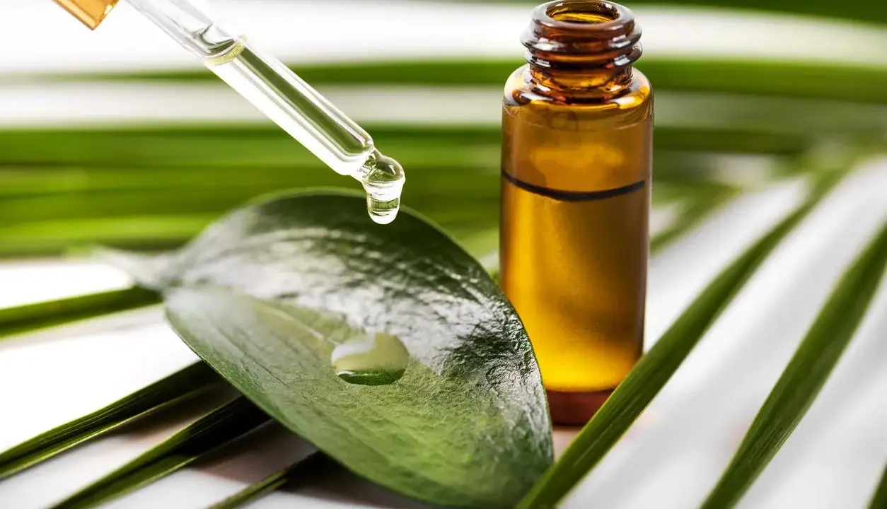 Goutte d'huile de tea tree acné tombant d'une pipette sur une feuille verte, à côté d'un flacon ambré.