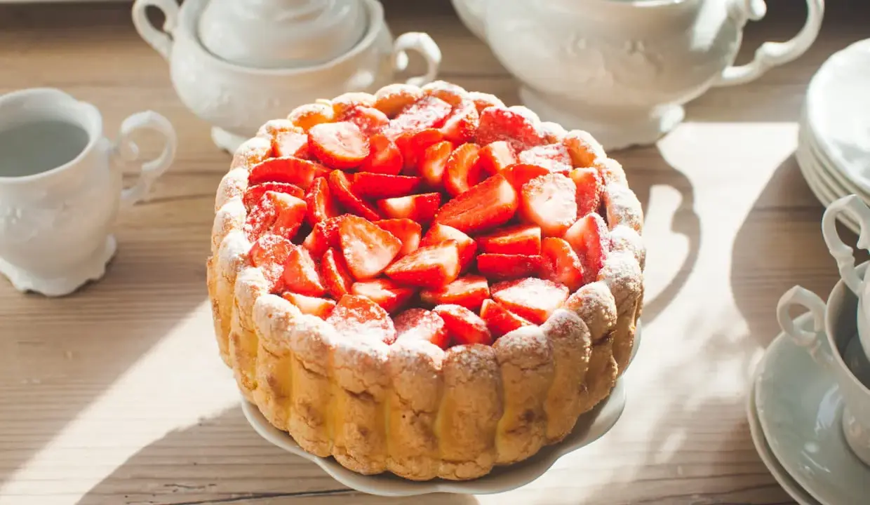Gâteau frais garni de fraises, entouré de biscuits cuillère et saupoudré de sucre glace. Une belle table de thé.