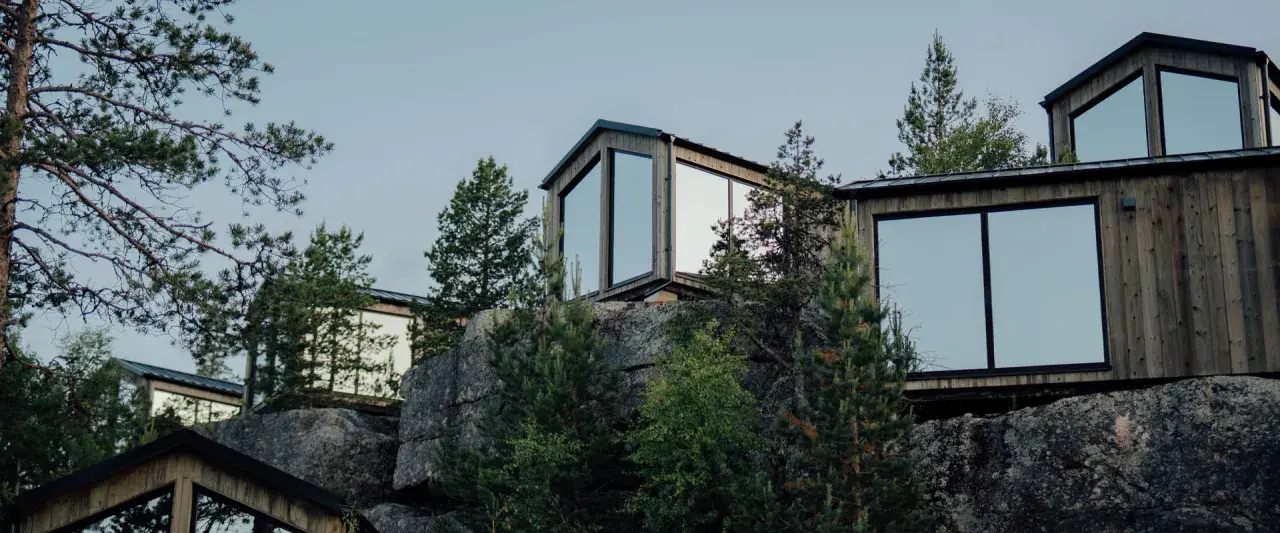 Moderna trähus med stora fönster klättrar uppför en stenig sluttning, omgivna av tallar. En idyllisk camping Lapland resort.