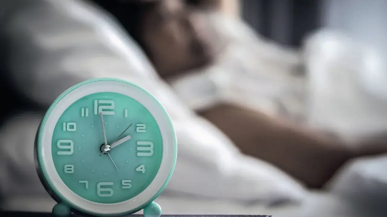 Ein Wecker neben einer schlafenden Person. Die Zeit ist kurz vor 2 Uhr. Ein Symbol für den zirkadianen Rhythmus.