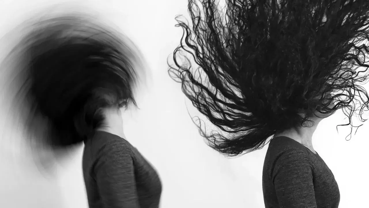 Dos cabezas con cabello largo y oscuro en movimiento, capturadas con un obturador fotográfico que crea un efecto de desenfoque dinámico.