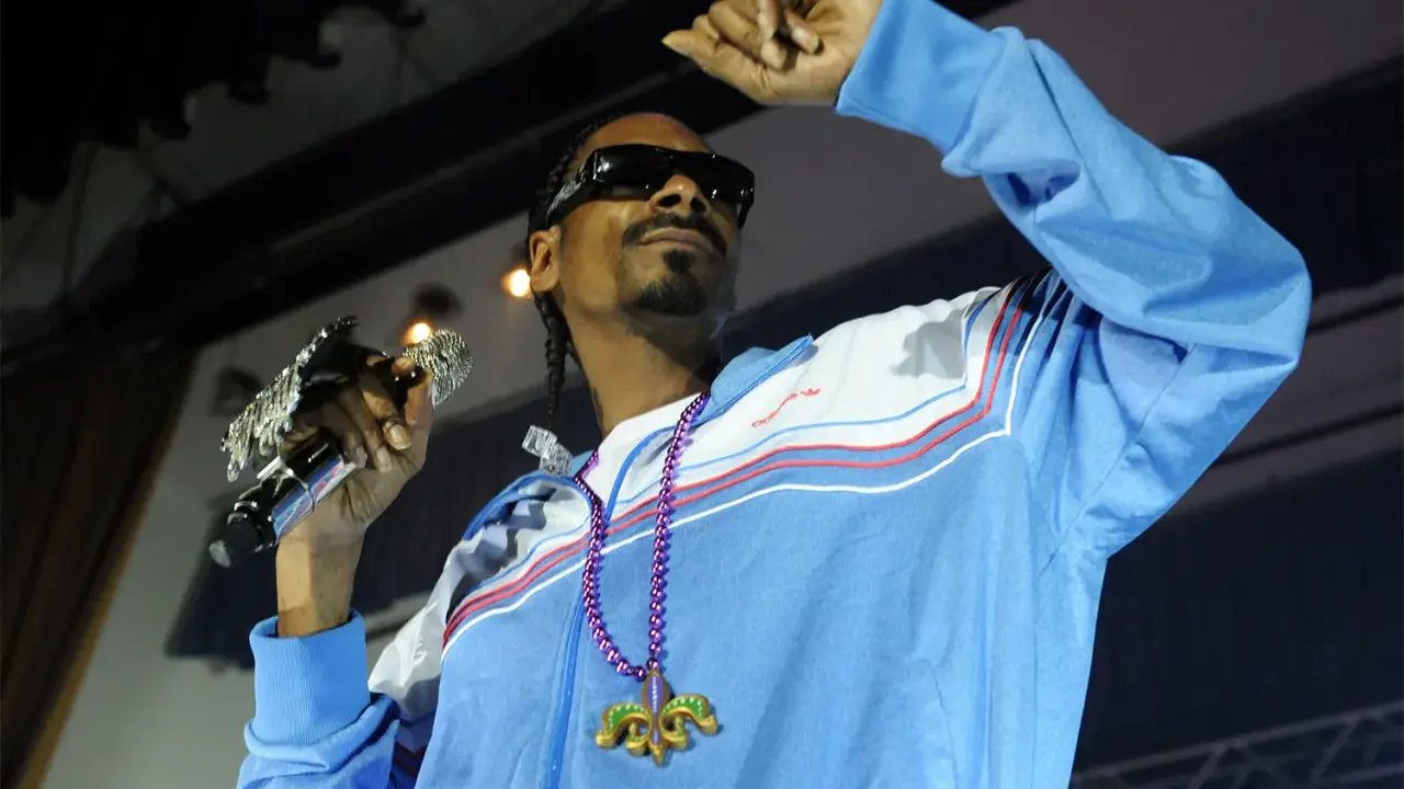 Snoop Dogg w błękitnej bluzie z naszyjnikiem, trzymający mikrofon. Ile pali? Tego nie wiemy, ale na pewno daje czadu na scenie!
