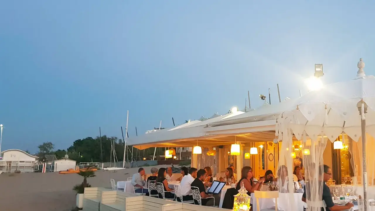 Serata in uno dei ristoranti della Riviera Romagnola, con tavoli apparecchiati sulla sabbia e luci soffuse.