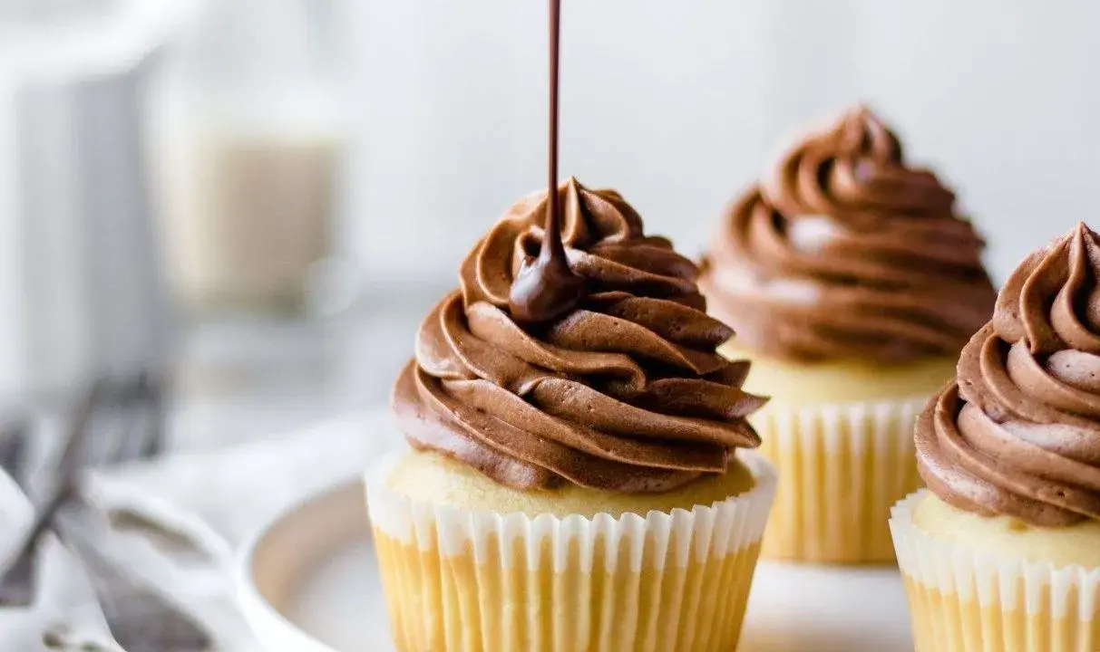 Glaçage onctueux de ganache montée mascarpone sur des cupcakes. Un filet de chocolat coule sur le glaçage.
