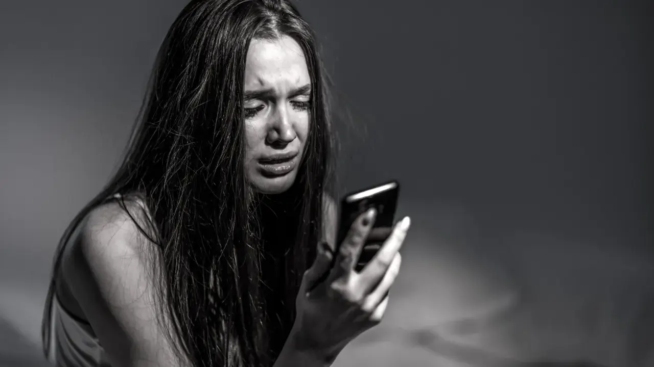 Ragazza piange guardando il telefono, vittima di revenge porn. La legge punisce chi diffonde immagini private senza consenso.