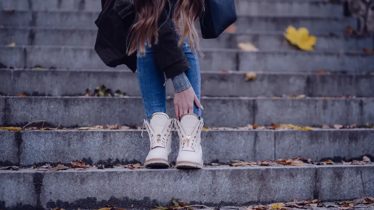 Kobieta w beżowych botkach na schodach, otoczona jesiennymi liśćmi.