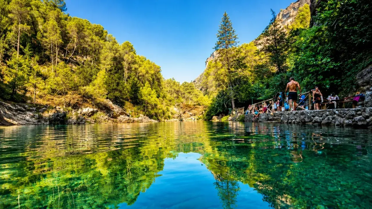Un refrescante charco del aceite, rodeado de vegetación exuberante y rocas, con gente disfrutando del día.