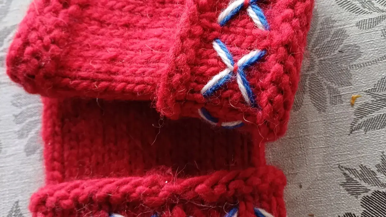 Närbild på röda, stickade vantar utan fingrar med korsstygn i vitt och blått. Perfekt för att virka vantar utan fingrar.