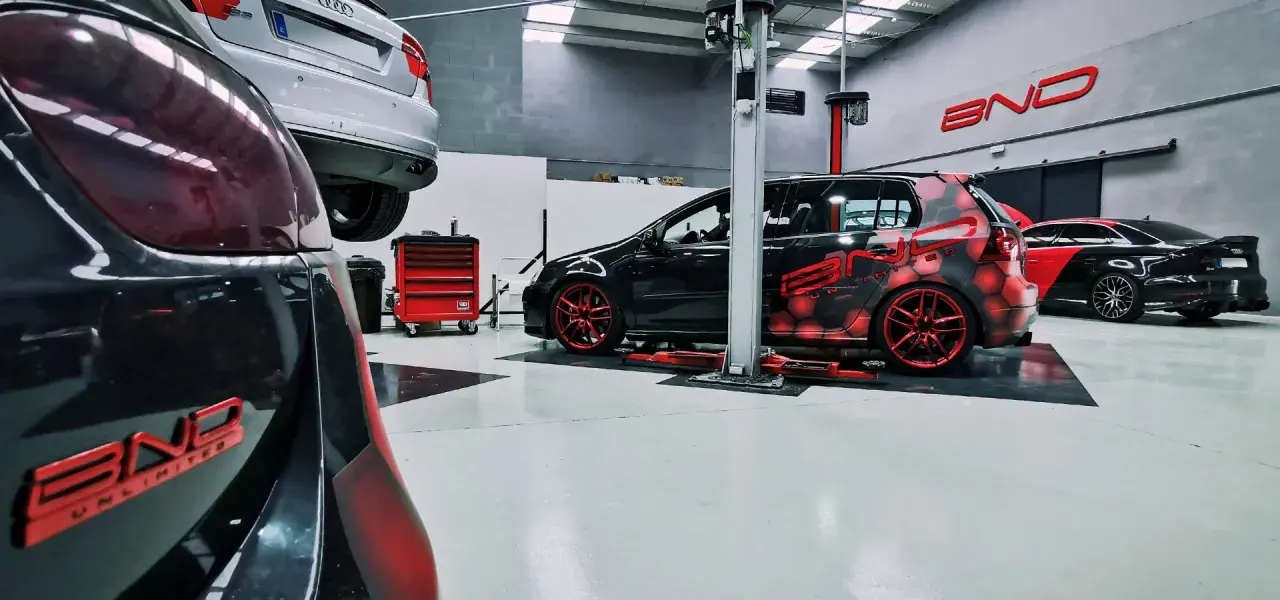 Taller con coches modificados. Uno negro con diseño de hexágonos rojos y llantas rojas, otro negro y rojo con alerón. Se pregunta cuánto cuesta reprogramar un coche.