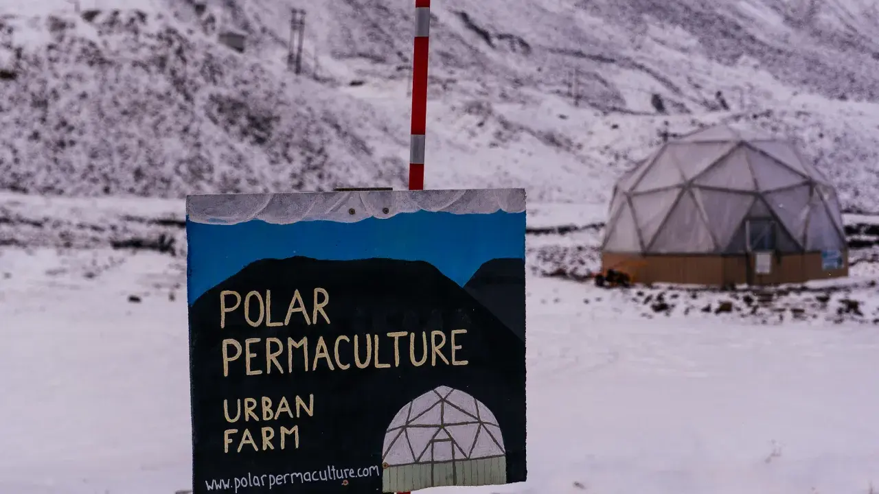 Panneau "Polar Permaculture Urban Farm" devant un dôme géodésique enneigé, rappelant la réserve mondiale de semences du Svalbard.