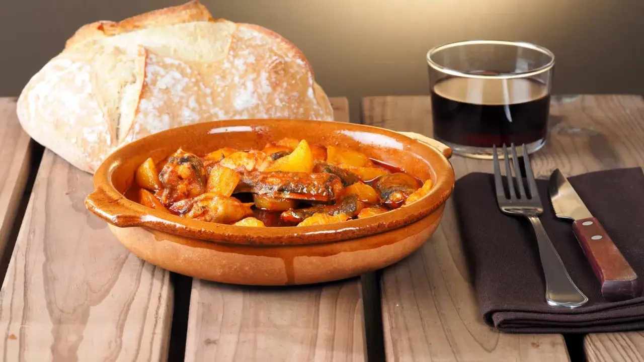 Un plato de all i pebre, con pan rústico y vino tinto, listo para disfrutar.