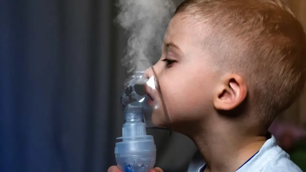 Chłopiec z maską inhalacyjną na twarzy, wdycha parę. Skuteczna inhalacja na katar u dziecka.