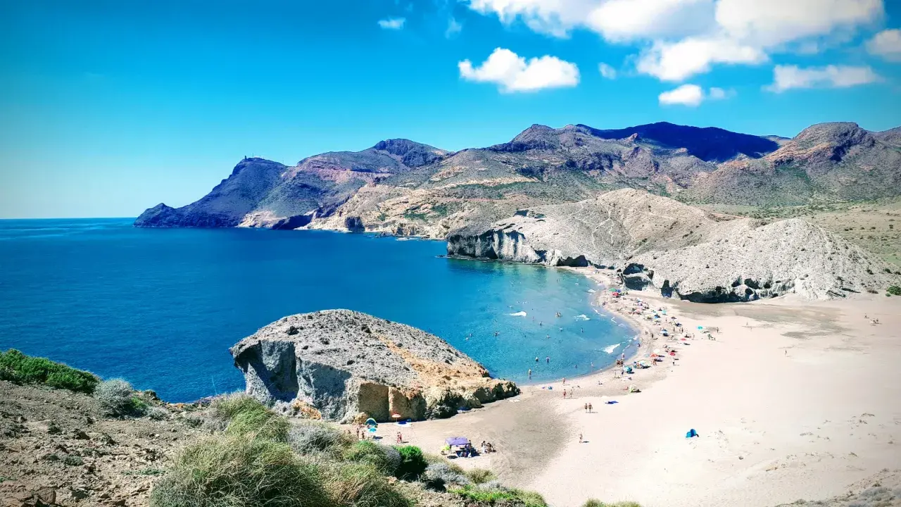 Sonnige playa de mónsul mit türkisfarbenem Wasser, Bergen und vielen Badegästen.
