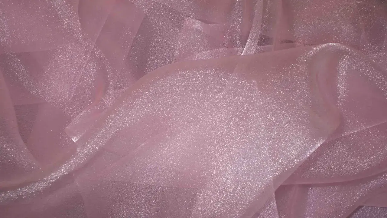 A shimmering pink organza fabric, with its sheer, crisp texture, drapes elegantly, catching the light.
