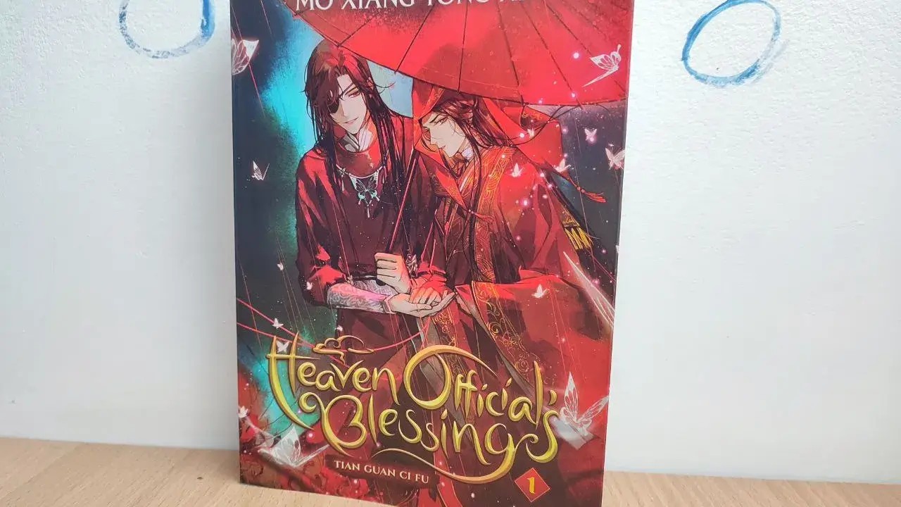 Okładka książki "Heaven Official's Blessing" z dwoma mężczyznami pod czerwonym parasolem.
