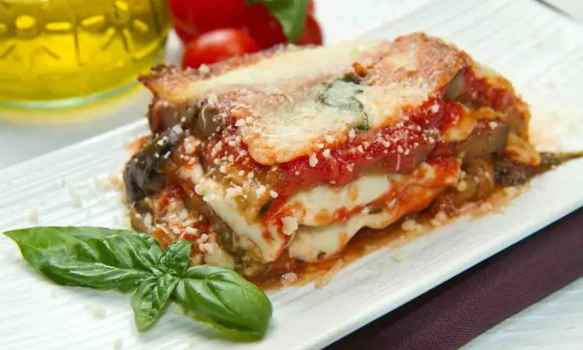 Una fetta di parmigiana di mare pugliese, con melanzane, pomodoro e mozzarella filante, guarnita con basilico fresco.