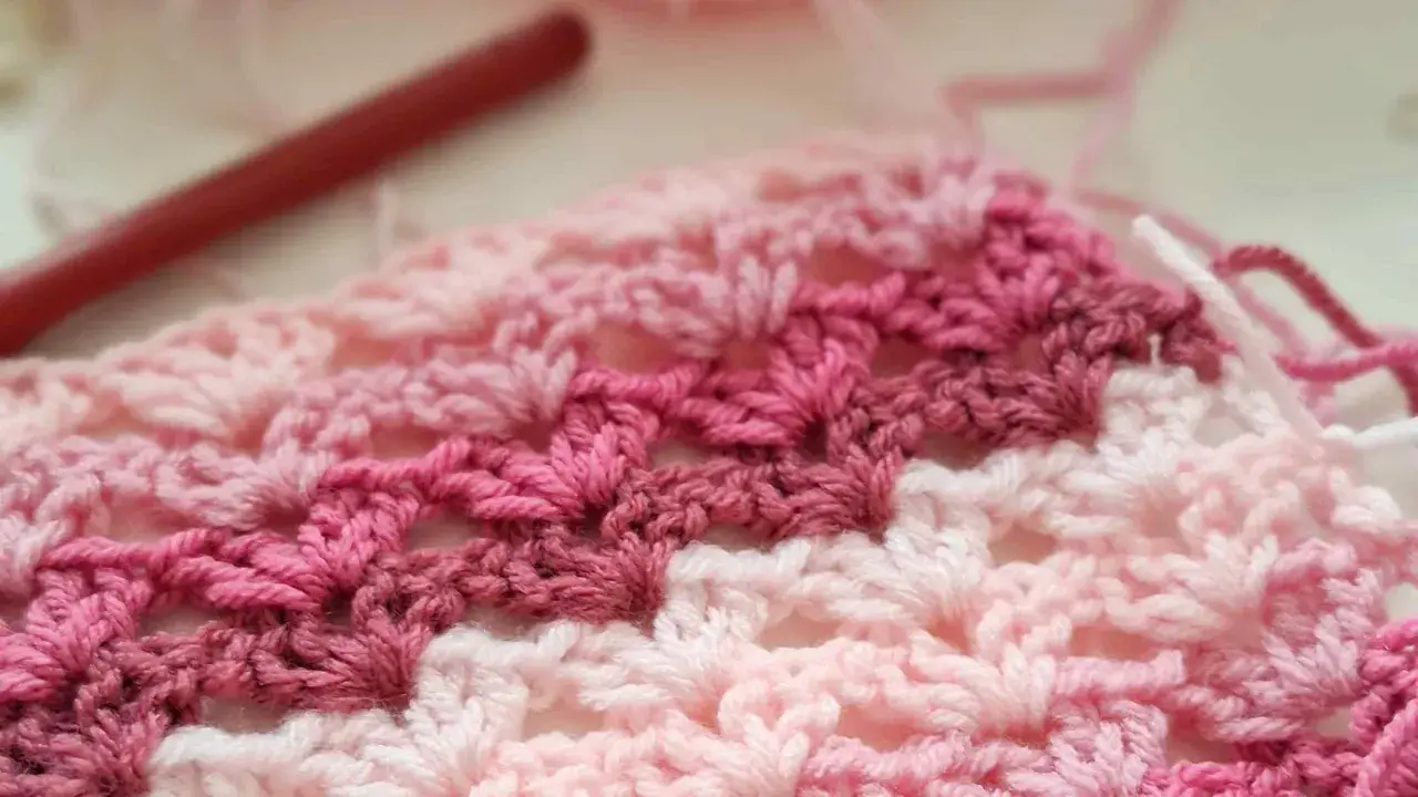 Tejido a crochet con hilo rosa y blanco. Un patrón de chaleco fácil en progreso, con un ganchillo rojo al fondo.