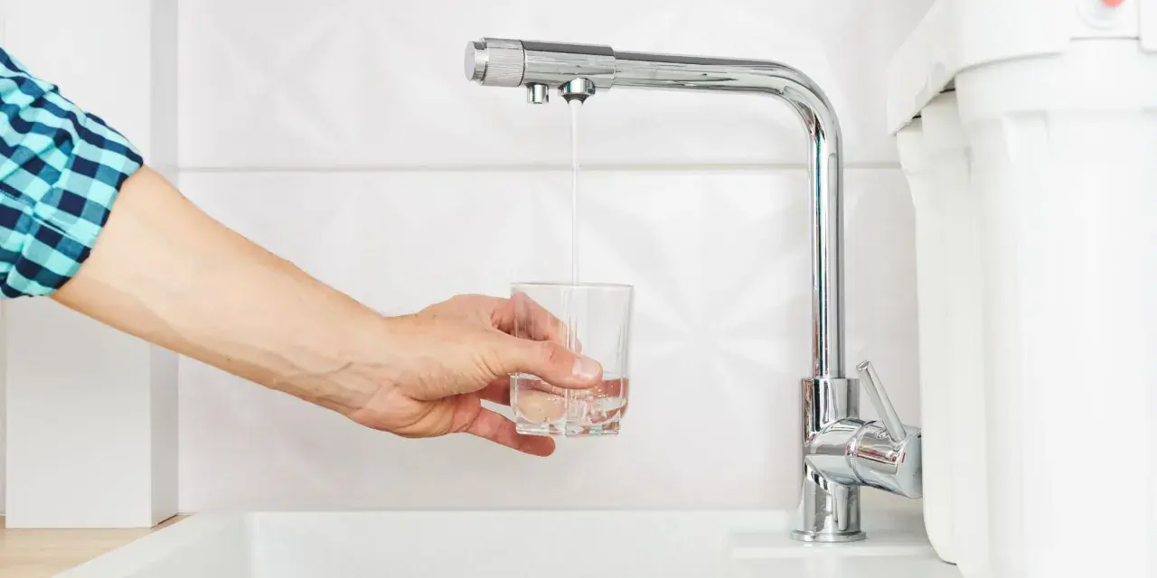 Main tenant rempli un verre d'eau sous un robinet de cuisine moderne, peut-être pour tester un nouveau joint mitigeur cuisine.