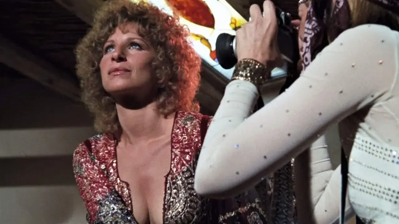 Barbra Streisand poses as Audrey Hepburn, dressed in a sparkly outfit, captures the moment with her camera.