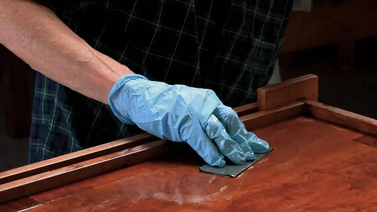 Mano enguantada lijando superficie de madera barnizada. El lijado es un paso clave para aplicar lac.