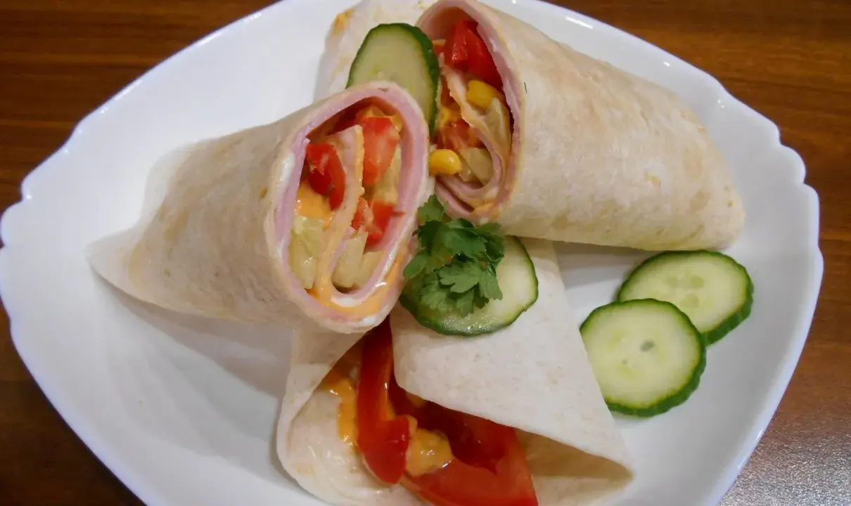 Pyszna tortilla z szynką, pomidorem, kukurydzą i ogórkiem, polana sosem. Idealna na szybki posiłek.