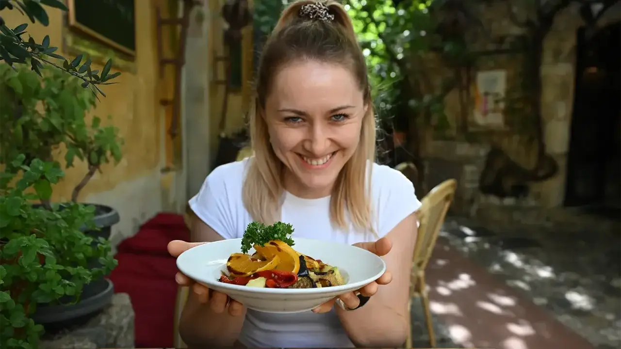 Uśmiechnięta kobieta prezentuje talerz pełen kolorowych warzyw, idealnych na dietę śródziemnomorską.