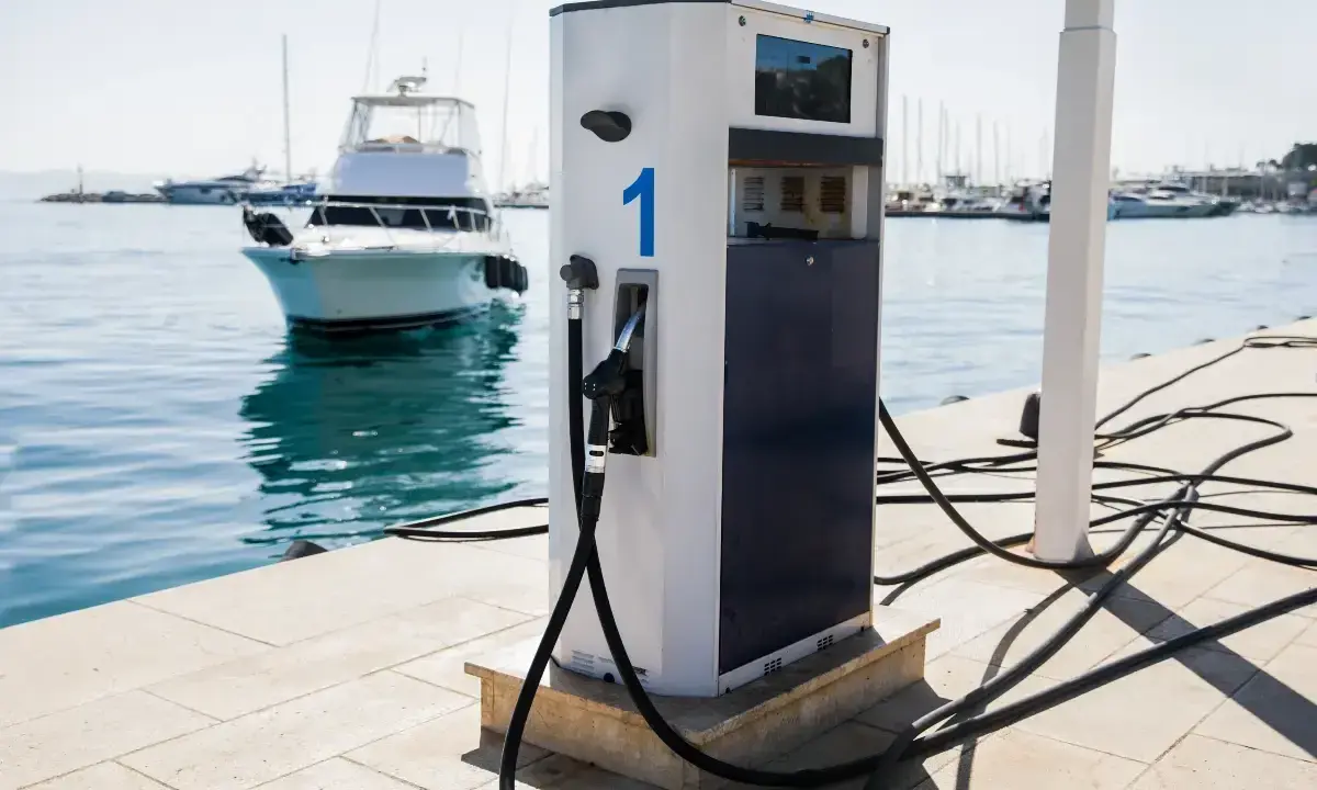 Borne de recharge pour bateaux, avec un tuyau prêt à l'emploi. L'eau bleue et les voiliers en arrière-plan rappellent que l'essence trop vieille n'est pas une option ici.