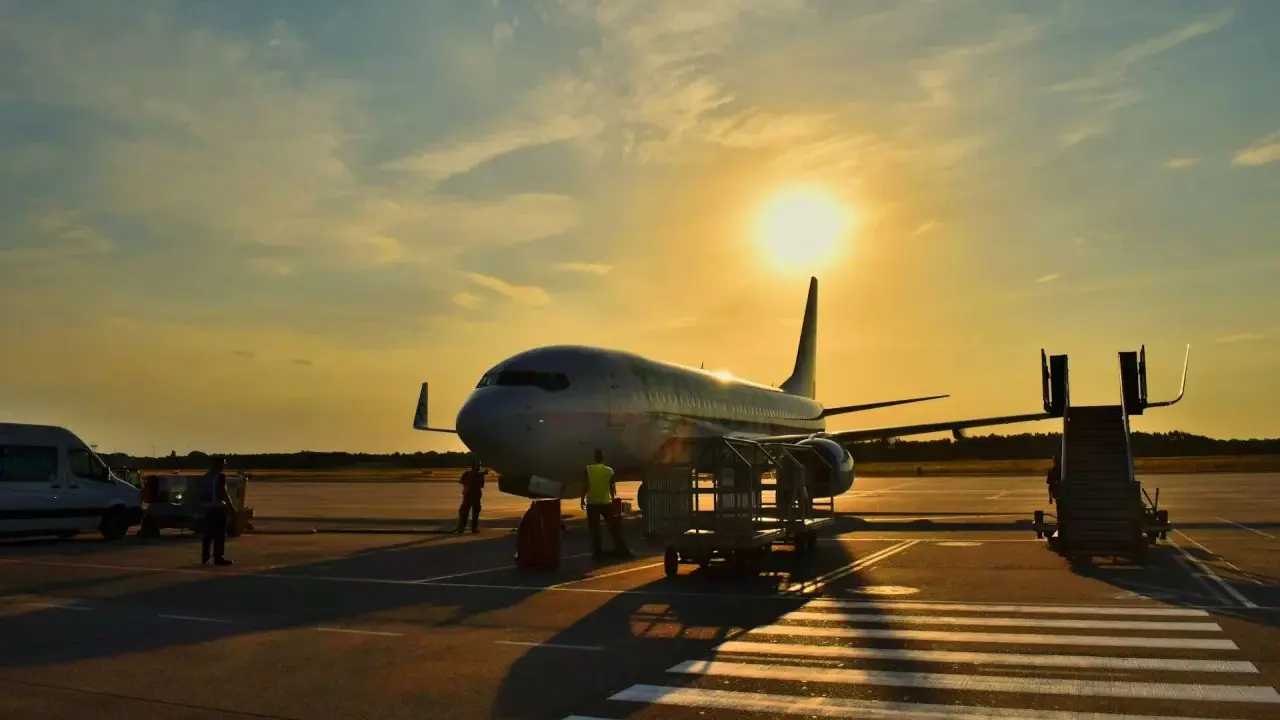 Samolot flydubai na lotnisku o zachodzie słońca. Pracownicy przygotowują bagaż rejestrowany, sprawdzając jego wymiary przed załadunkiem.