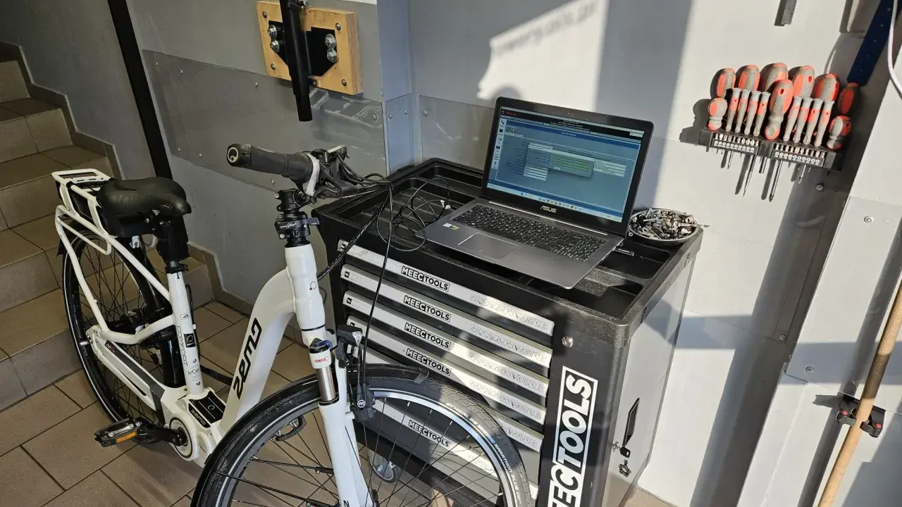 Profesjonalna naprawa rowerów elektrycznych w warsztacie. Biały rower elektryczny, laptop z oprogramowaniem diagnostycznym i zestaw narzędzi.